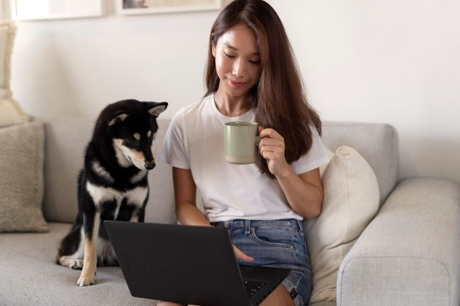 Image of girl sitting on couch with laptop and a dog watching next to her